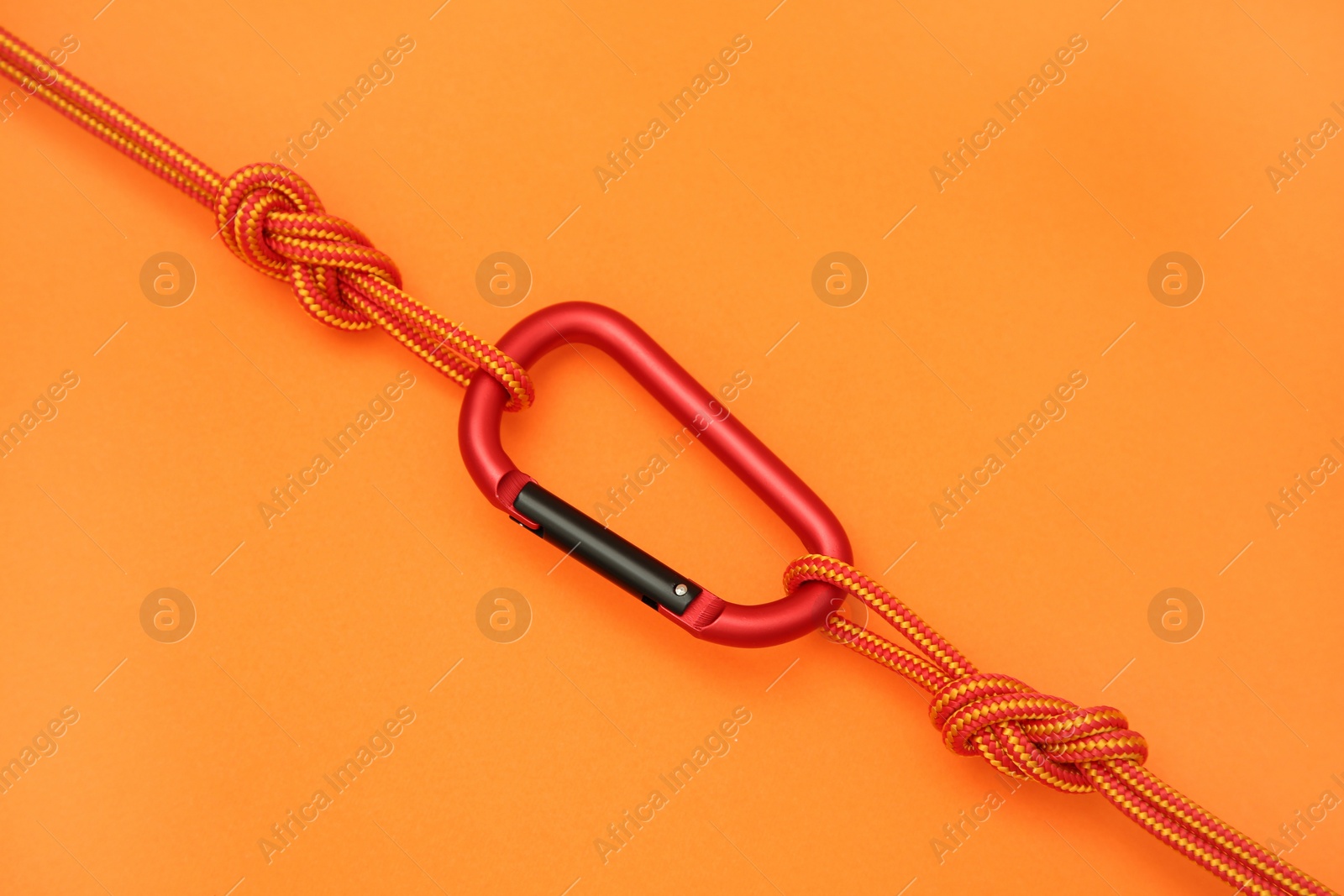 Photo of One metal carabiner with ropes on orange background, top view