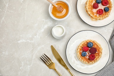 Delicious breakfast with waffles, honey and berries on light table, flat lay. Space for text