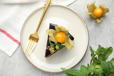 Piece of tasty cake decorated with physalis fruit on light grey table, flat lay