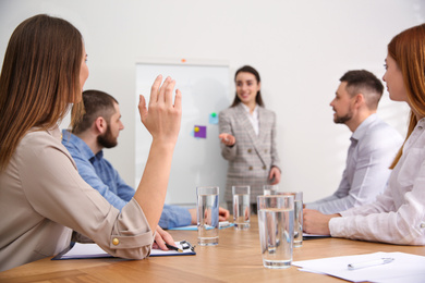 Young woman raising hand to ask question at business training in conference room