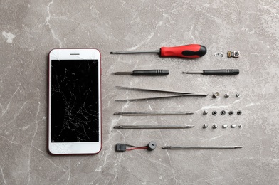 Photo of Flat lay composition with broken mobile phone and repair tools on table