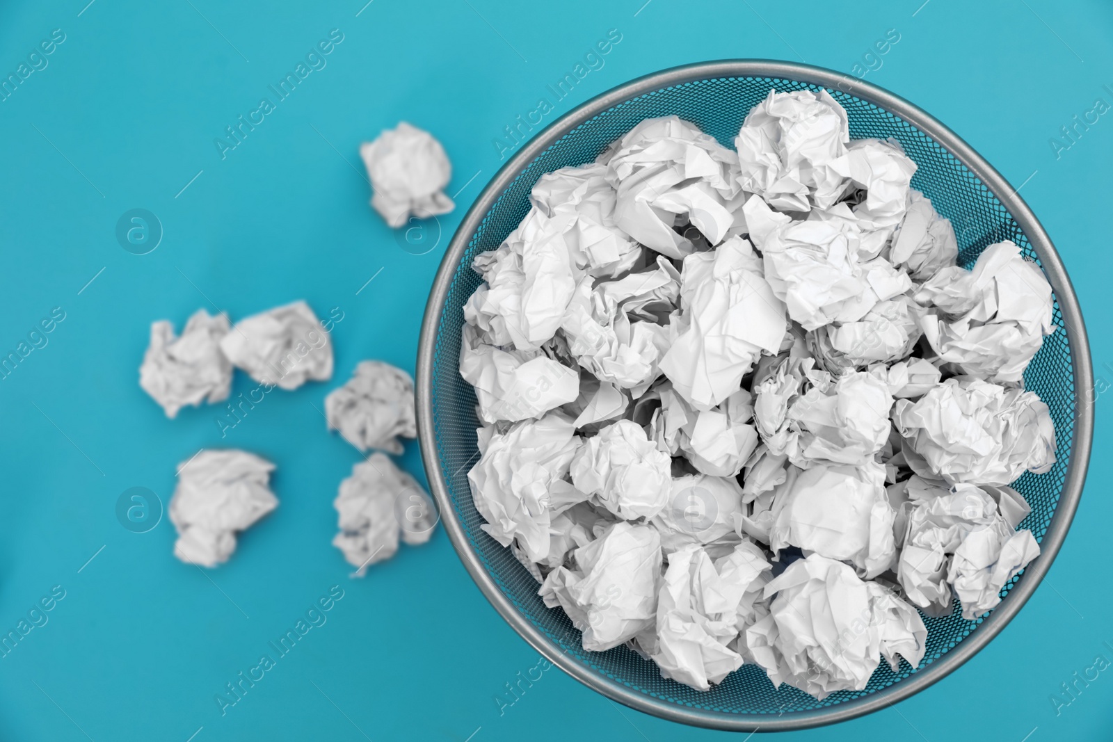 Photo of Metal bin with crumpled paper on color background, top view. Space for text