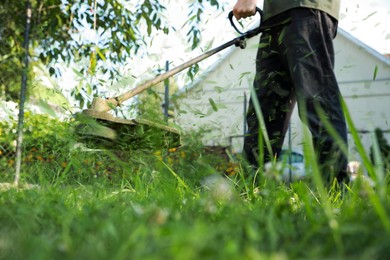 Man cutting green grass with string trimmer outdoors, closeup