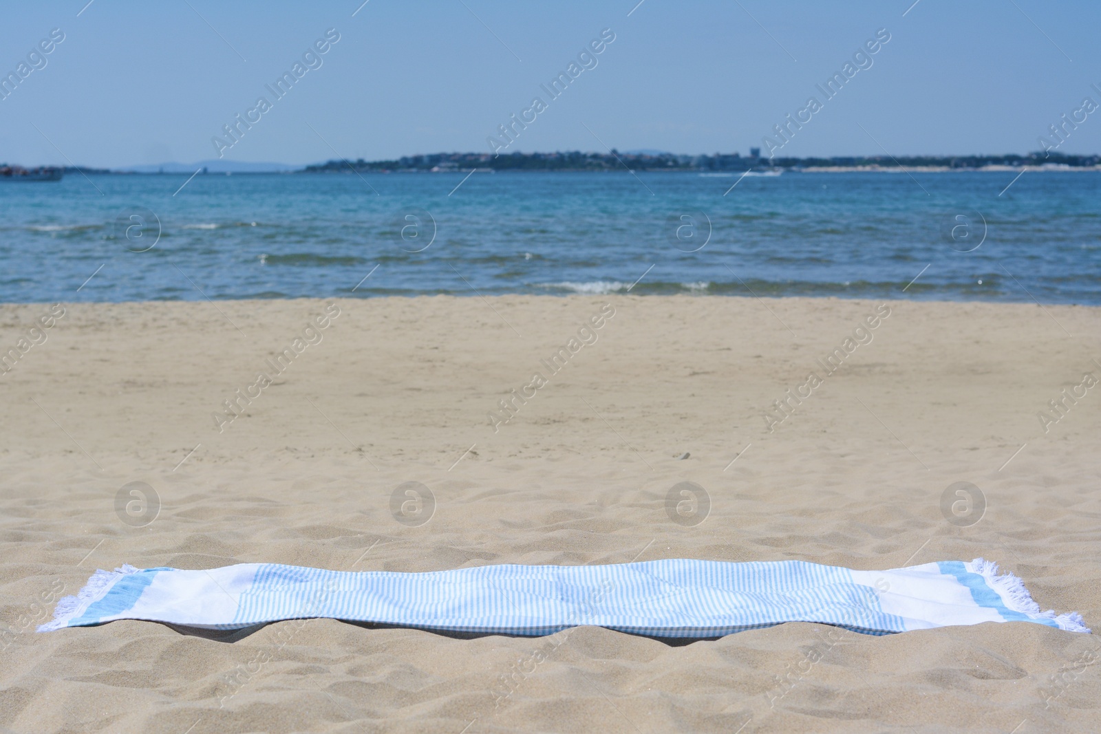 Photo of Light blue towel on sandy beach near sea, space for text