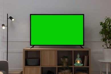 Image of Modern TV on cabinet, floor lamp and beautiful houseplants near light wall indoors. Interior design