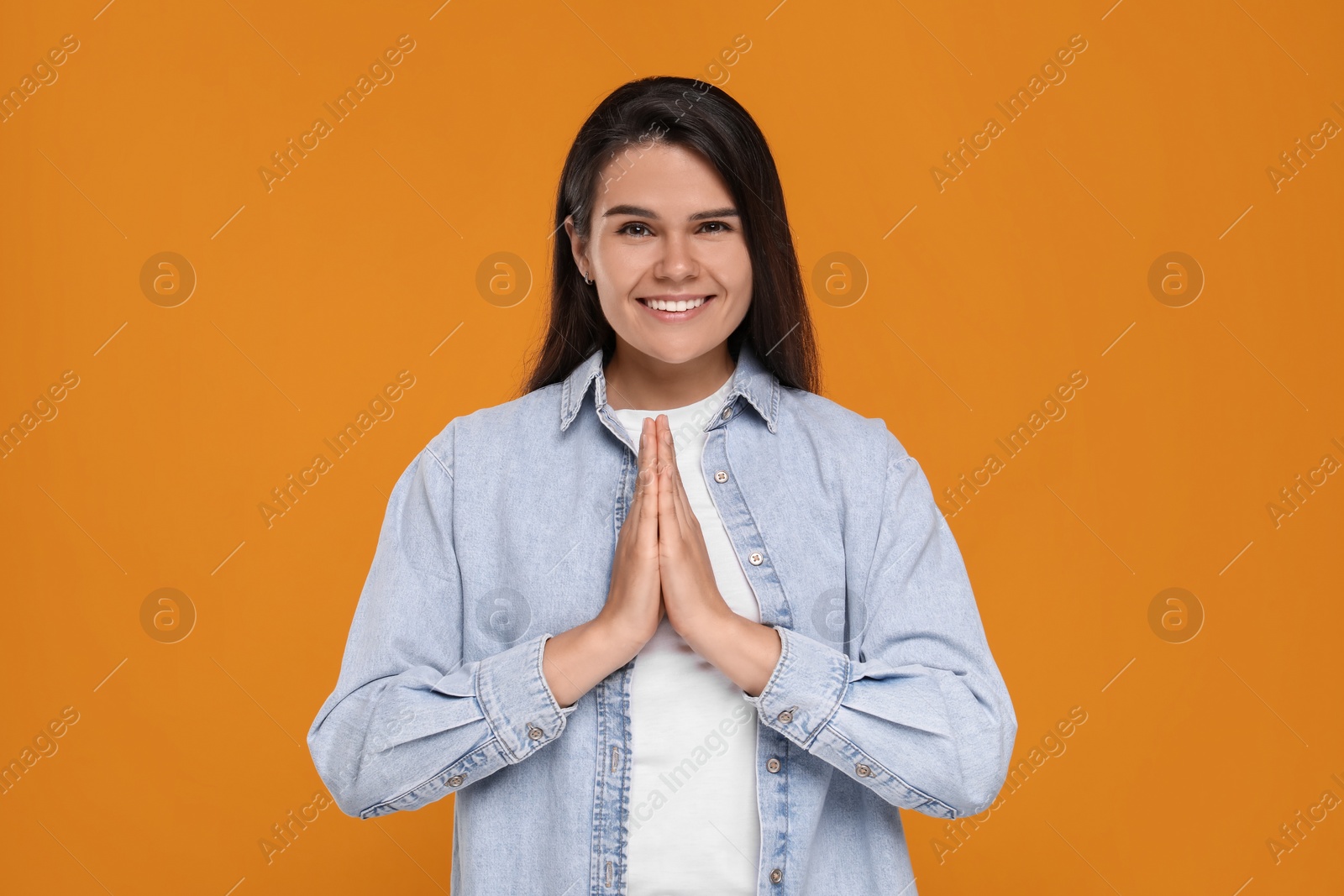 Photo of Thank you gesture. Beautiful grateful woman with hands clasped together on orange background