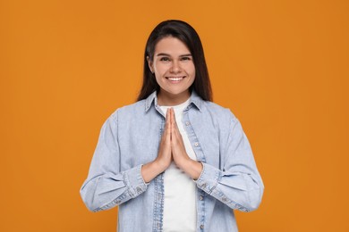 Photo of Thank you gesture. Beautiful grateful woman with hands clasped together on orange background