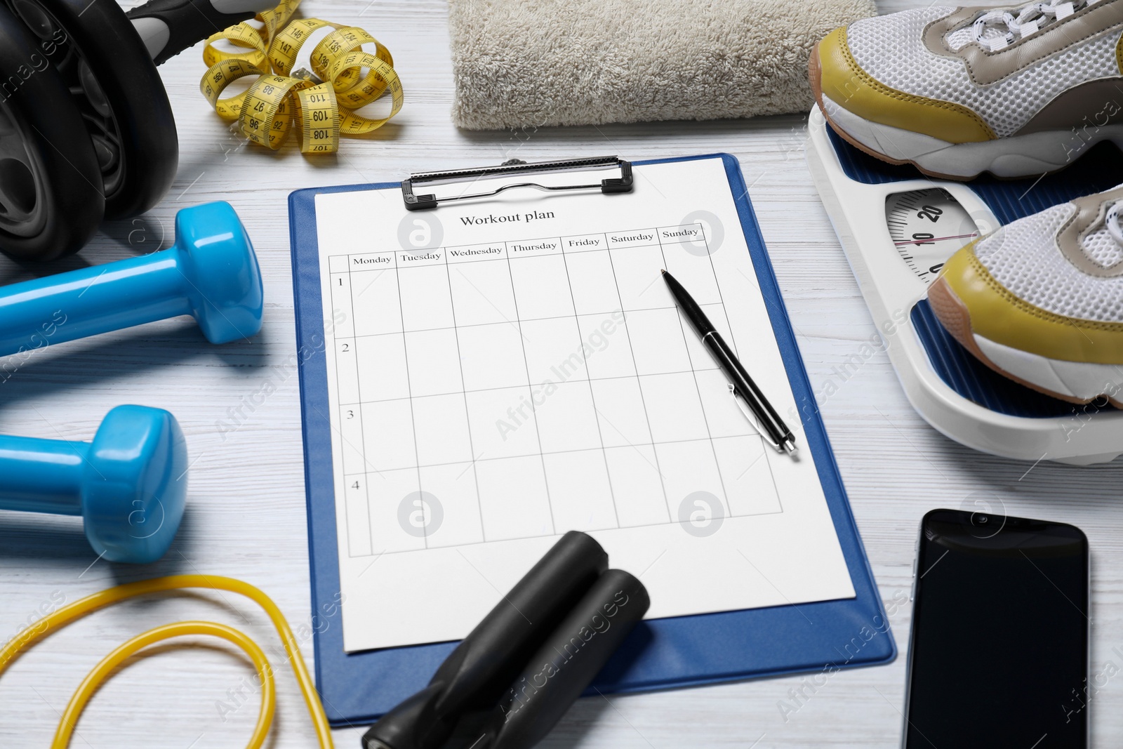 Photo of Clipboard with workout plan, smartphone and sports equipment on white wooden table. Personal training