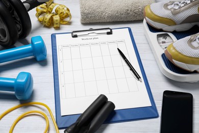Photo of Clipboard with workout plan, smartphone and sports equipment on white wooden table. Personal training