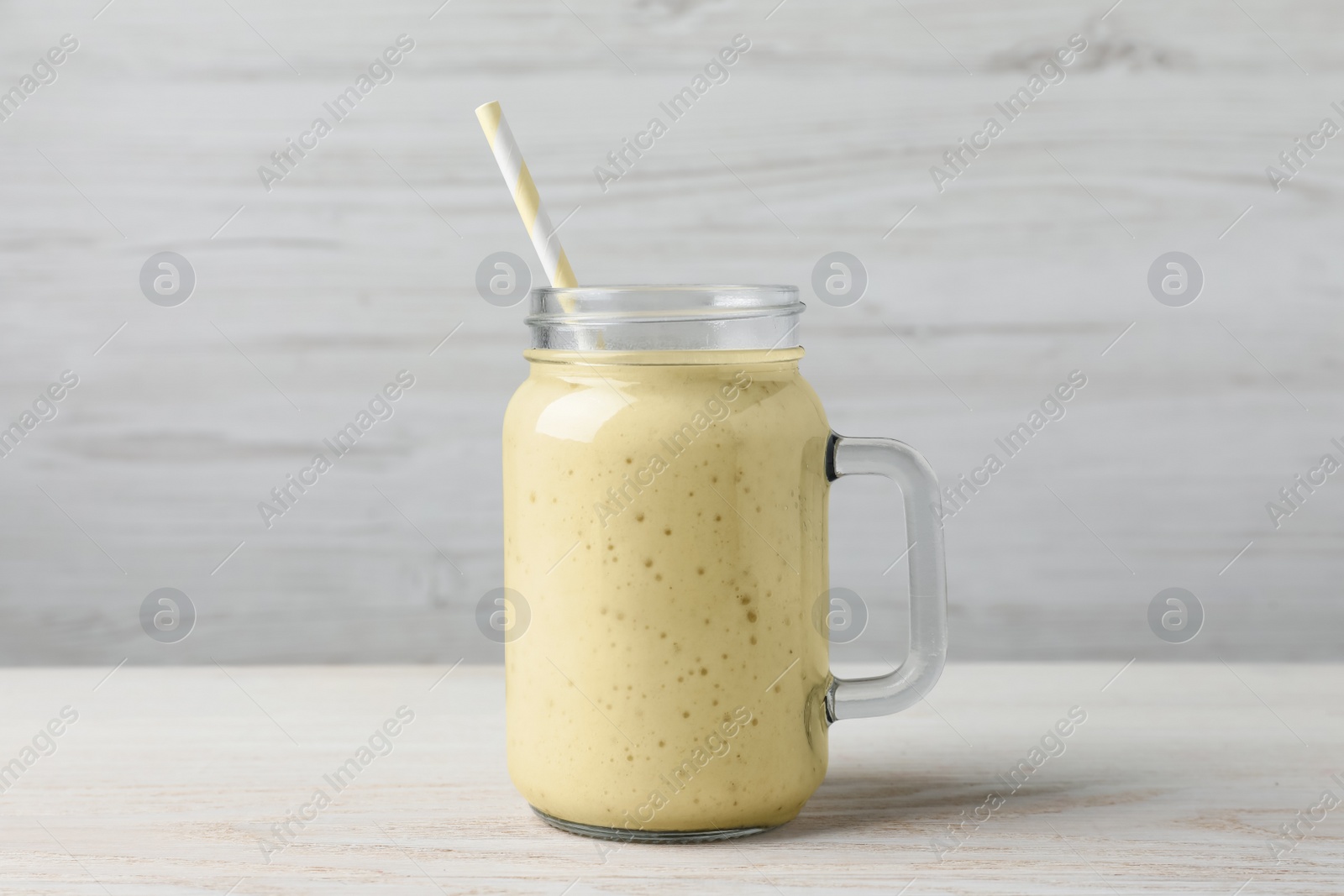 Photo of Mason jar with delicious fruit smoothie on white wooden table