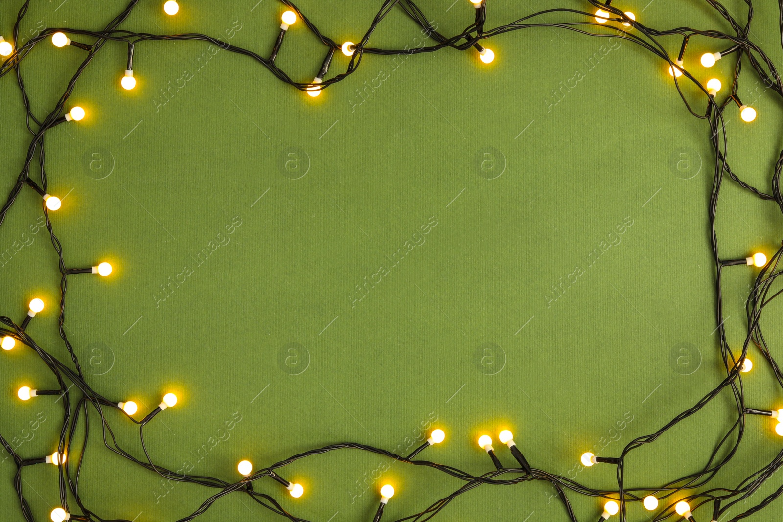 Photo of Frame made with Christmas lights on green background, top view. Space for text