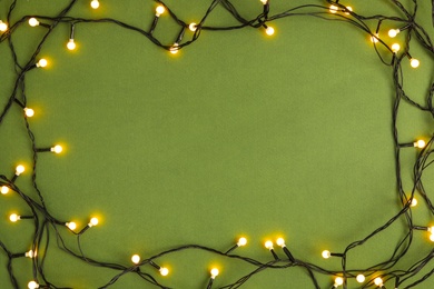 Photo of Frame made with Christmas lights on green background, top view. Space for text