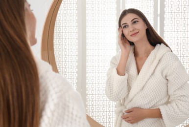 Young woman near mirror in bathroom. Skin care