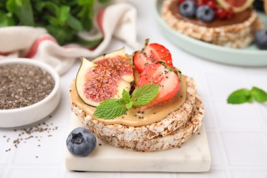 Photo of Tasty crispbreads with peanut butter, figs and berries on light table