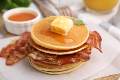 Pouring honey onto delicious pancakes with bacon at table, closeup