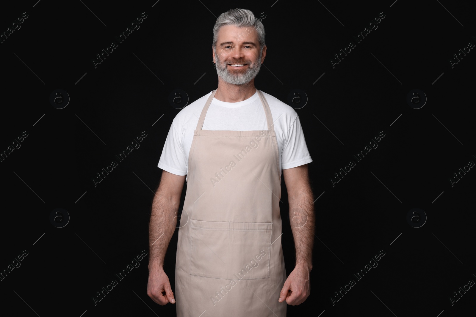 Photo of Happy man wearing kitchen apron on black background. Mockup for design