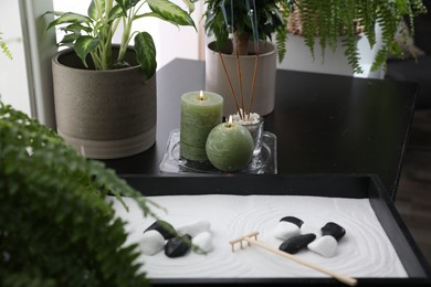 Photo of Candles and incense sticks near miniature zen garden on black table