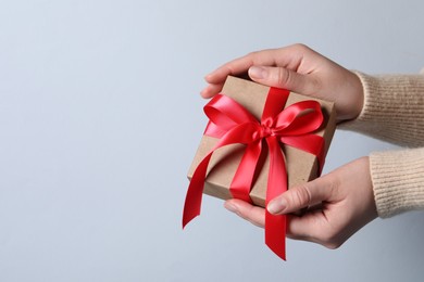 Woman holding gift box with red bow on light grey background, closeup. Space for text