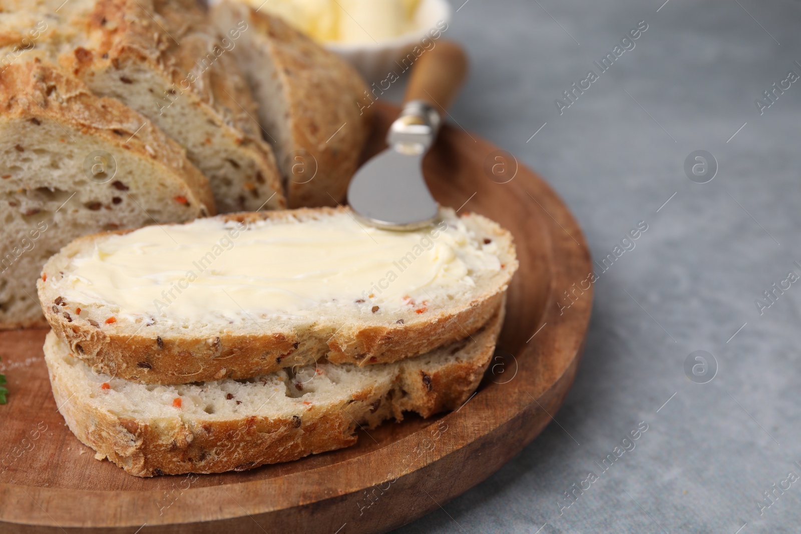 Photo of Tasty bread with butter and knife on grey textured table, closeup. Space for text