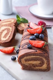 Photo of Tasty chocolate cake roll with cream and berries on board