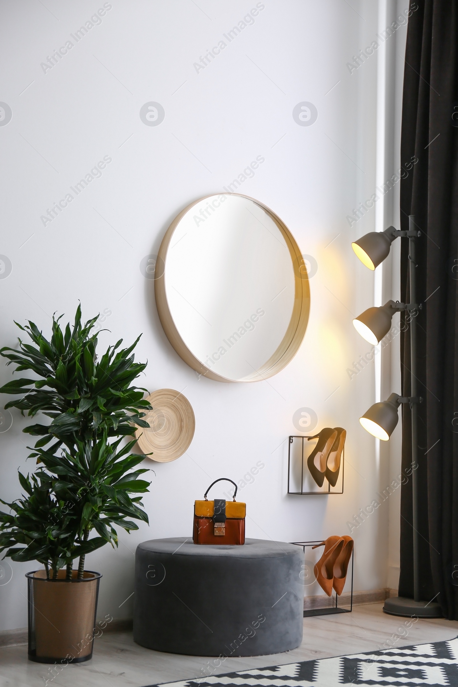 Photo of Hallway interior with big round mirror and ottoman chair near white wall