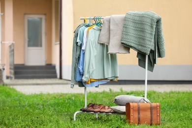 Photo of Clothing rack with different garments in yard, space for text. Garage sale