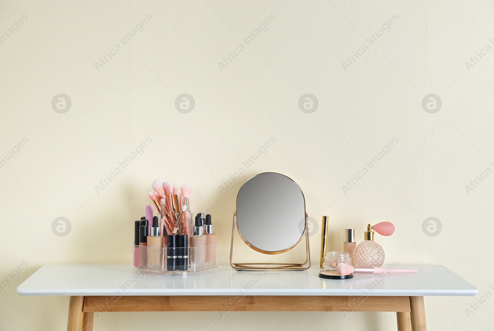 Photo of Mirror and makeup products on white table near light wall. Space for text