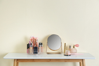 Mirror and makeup products on white table near light wall. Space for text