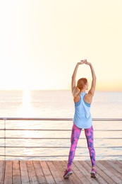 Photo of Young woman doing fitness exercises on pier in morning