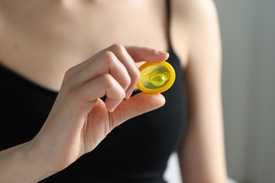 Photo of Woman holding unpacked condom on light background, closeup. Safe sex