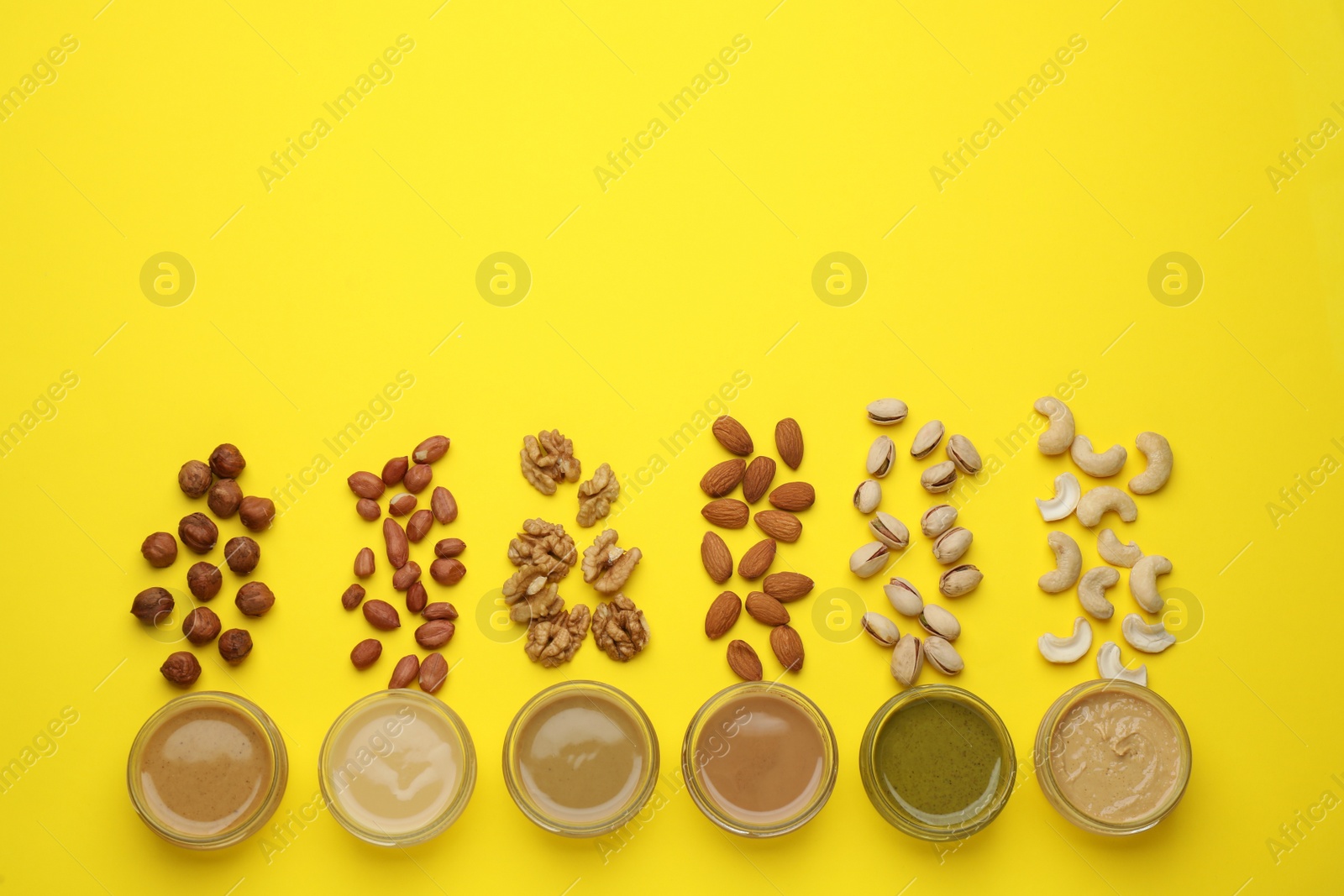 Photo of Different types of nut butter and ingredients on yellow background, flat lay. Space for text