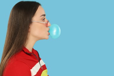 Photo of Beautiful young woman blowing bubble gum on light blue background. Space for text