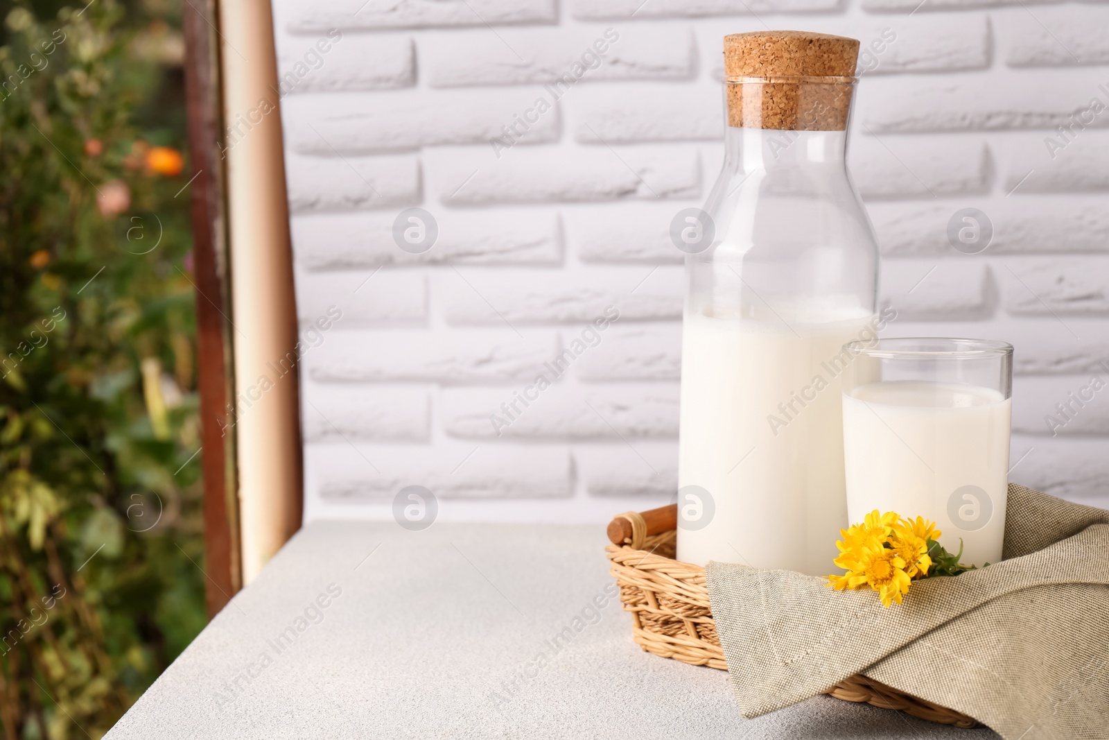 Photo of Glass and bottle of fresh milk on table against white brick wall. Space for text