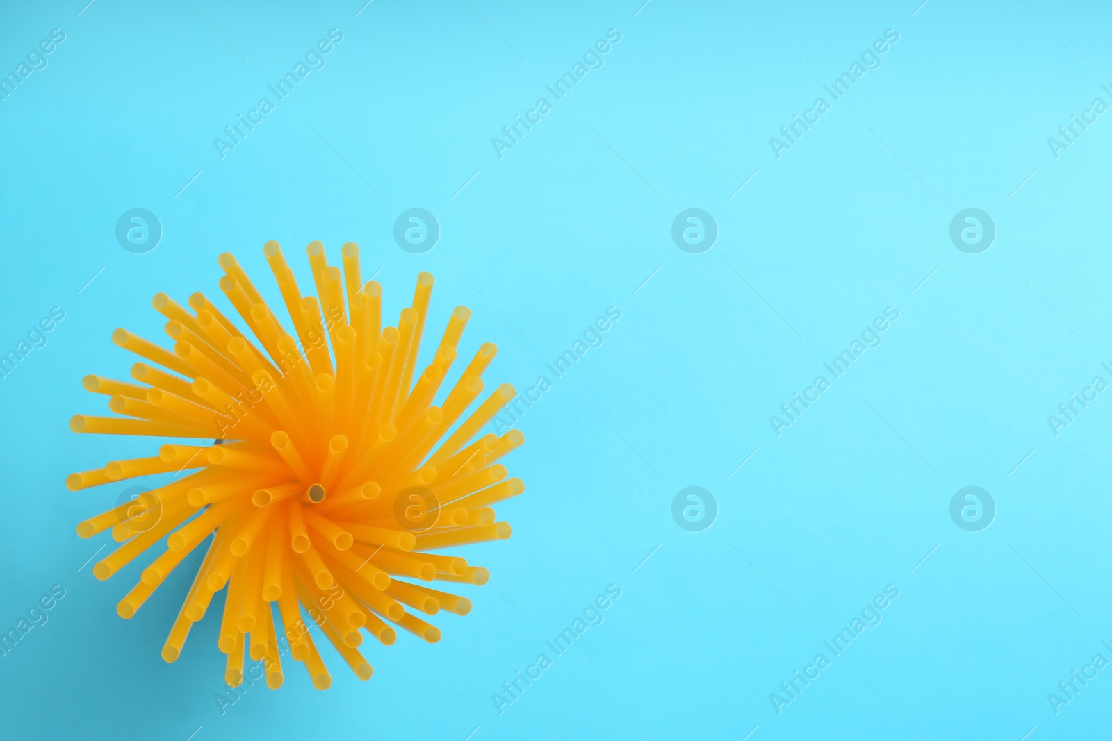 Photo of Orange plastic drinking straws on light blue background, top view. Space for text