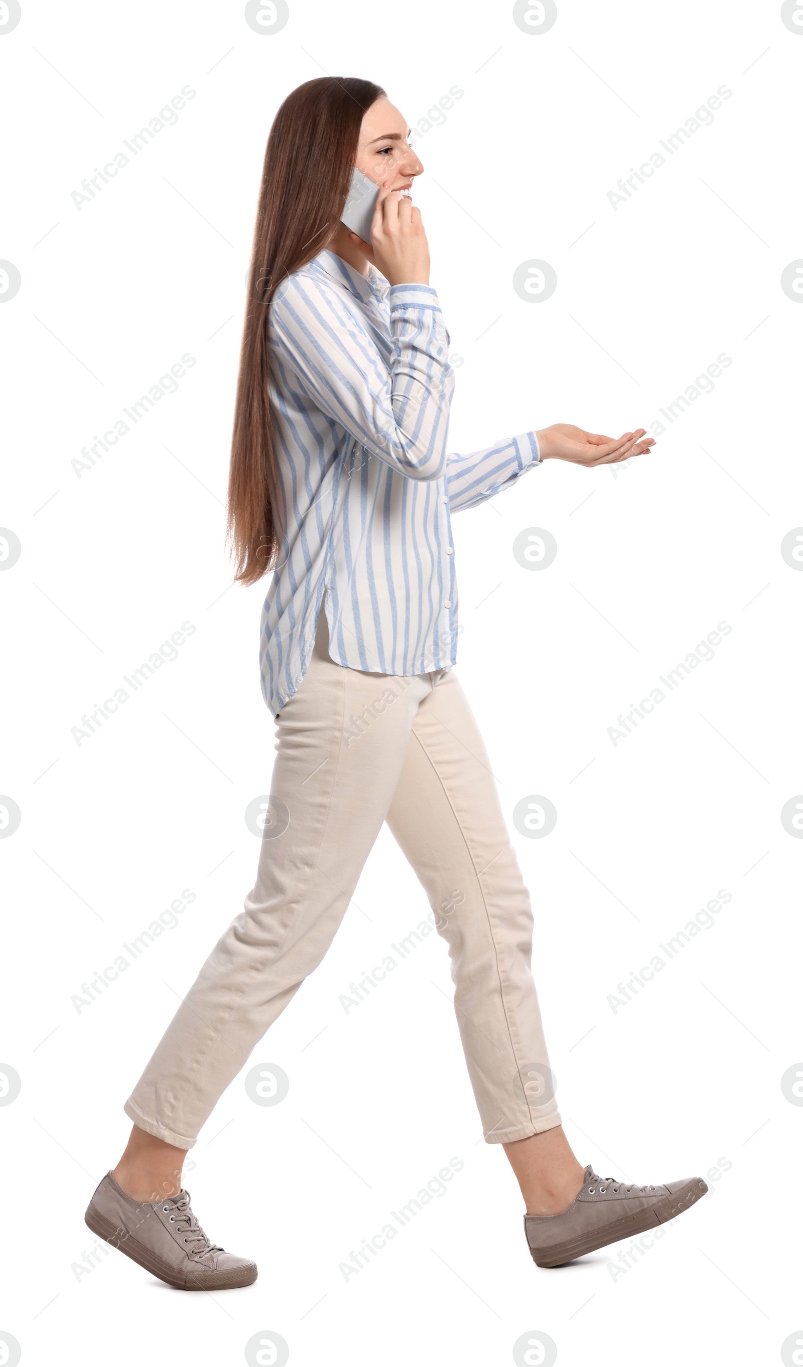 Photo of Young woman in casual outfit talking on smartphone while walking against white background