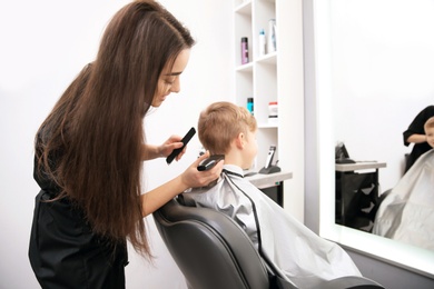 Professional female hairdresser working with little boy in salon