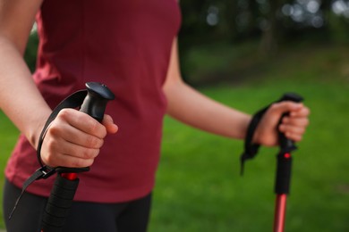 Photo of Young woman practicing Nordic walking with poles outdoors, closeup