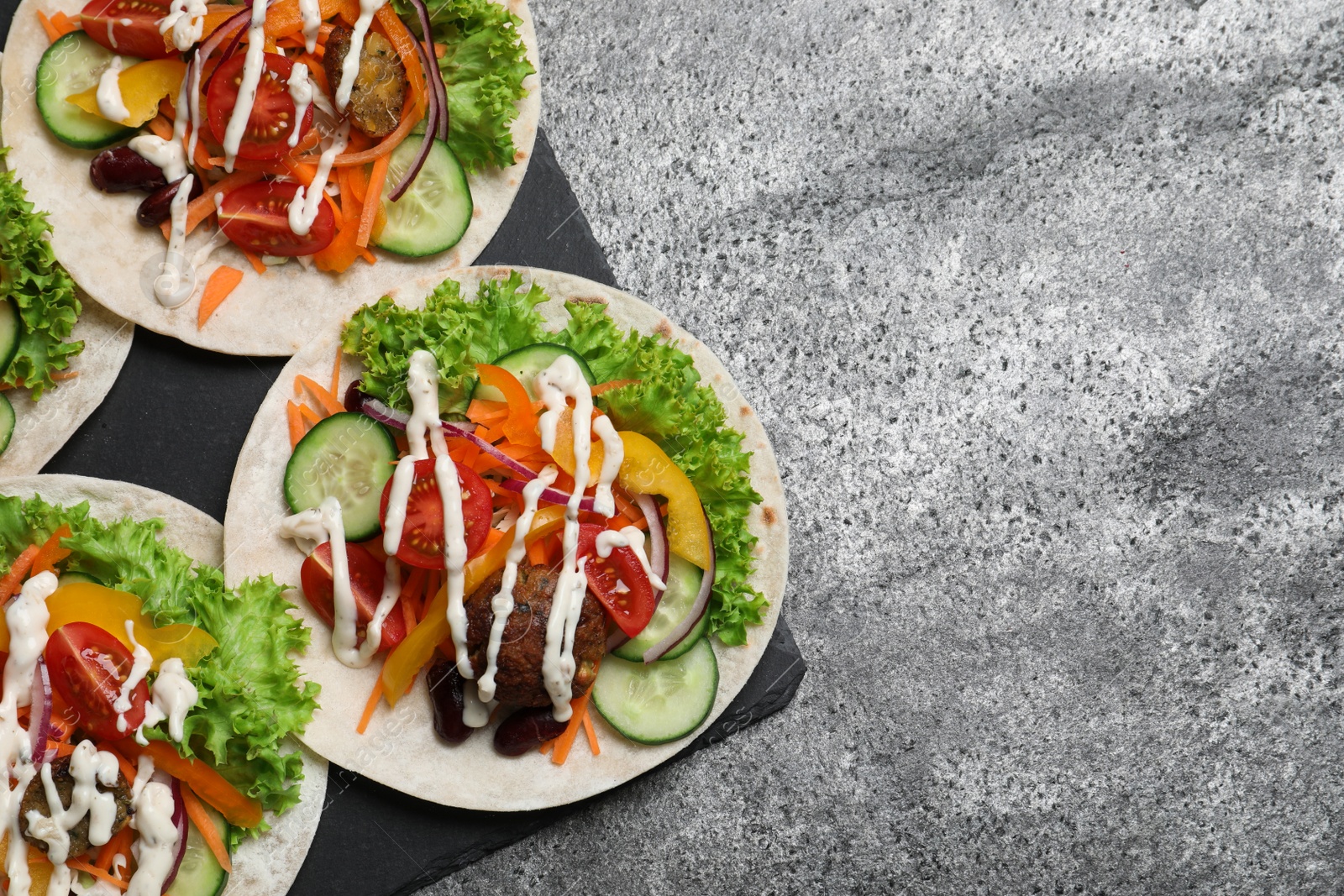 Photo of Many delicious vegetarian tacos served on grey table, flat lay. Space for text