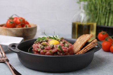 Photo of Tasty beef steak tartare served with yolk, capers and bread on light grey table