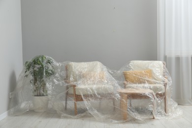 Photo of Stylish chairs, table and houseplant covered with plastic film at home
