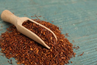 Scoop with dry rooibos leaves on light blue wooden table, space for text