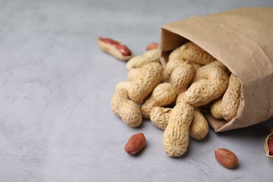 Photo of Paper bag with fresh unpeeled peanuts on grey table, closeup. Space for text