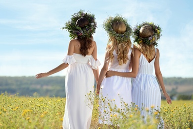 Young women wearing wreaths made of flowers in field on sunny day, back view