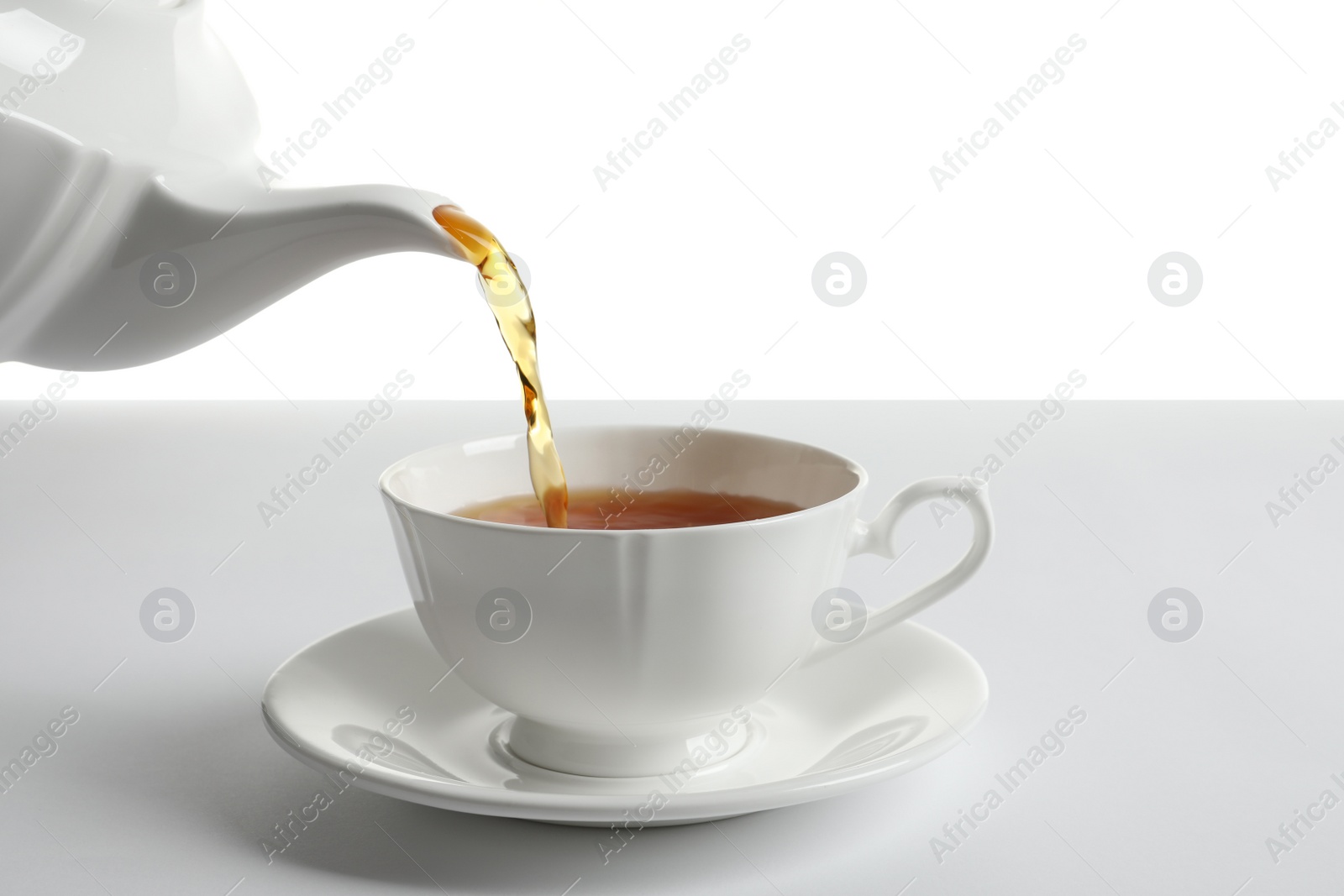 Photo of Pouring hot tea into porcelain cup on white background