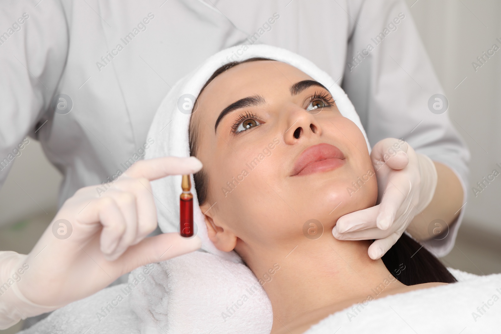 Photo of Professional cosmetologist holding skincare ampoule while working with client in clinic, closeup