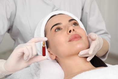 Professional cosmetologist holding skincare ampoule while working with client in clinic, closeup