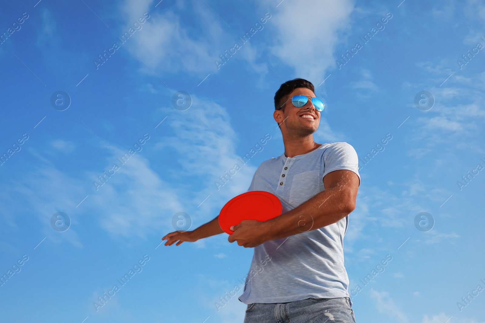 Photo of Happy man throwing flying disk against blue sky on sunny day, low angle view