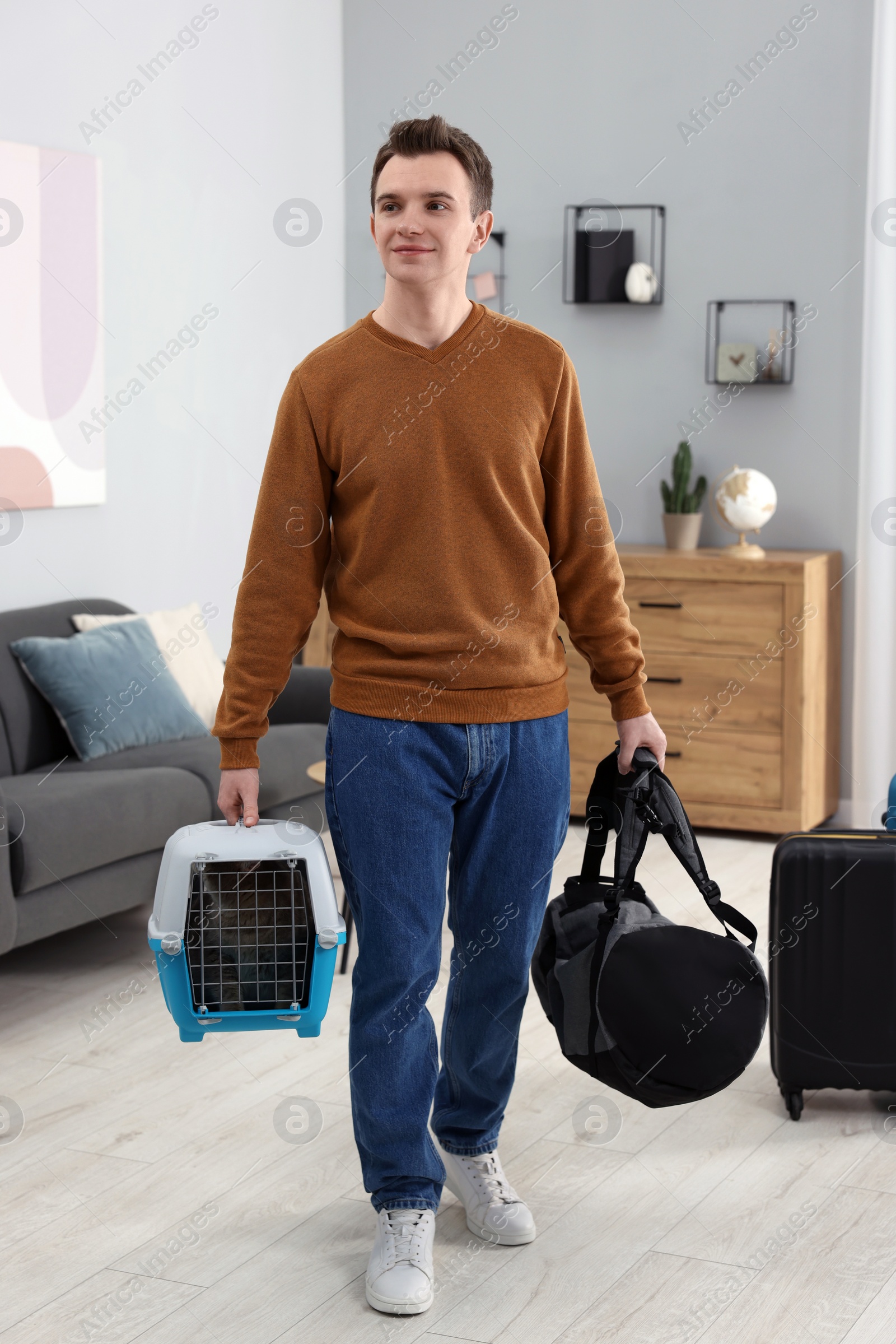 Photo of Travel with pet. Man holding carrier with cute cat and bag at home