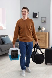 Photo of Travel with pet. Man holding carrier with cute cat and bag at home