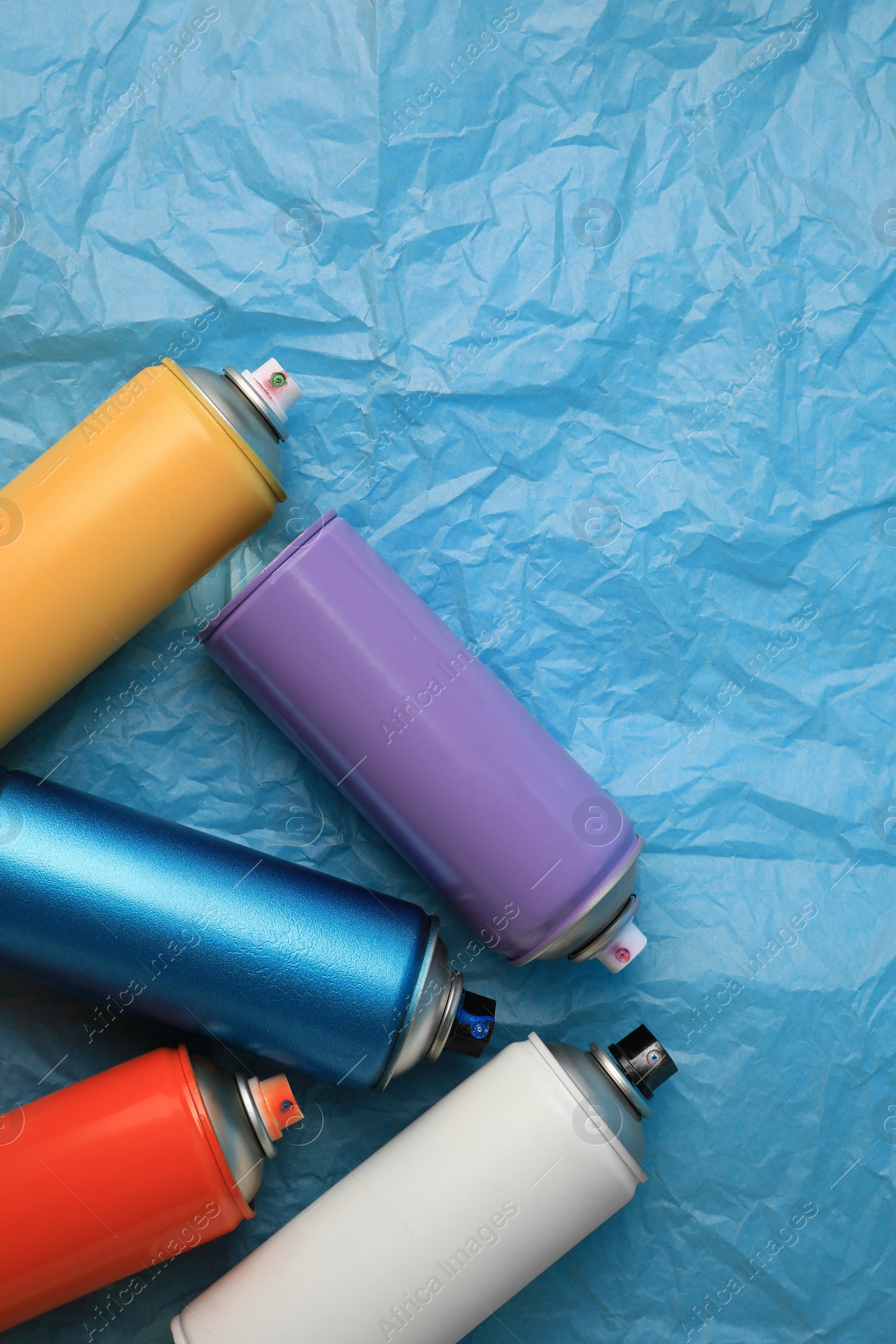 Photo of Cans of different graffiti spray paints on light blue crumpled paper, flat lay. Space for text